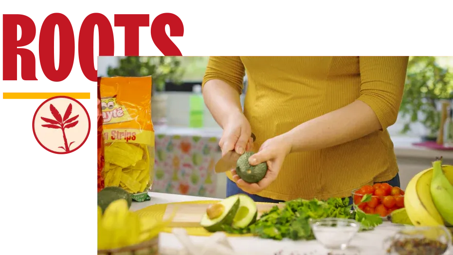 Woman preparing fresh vegetables and avocado in a kitchen with Mayte plantain chips nearby