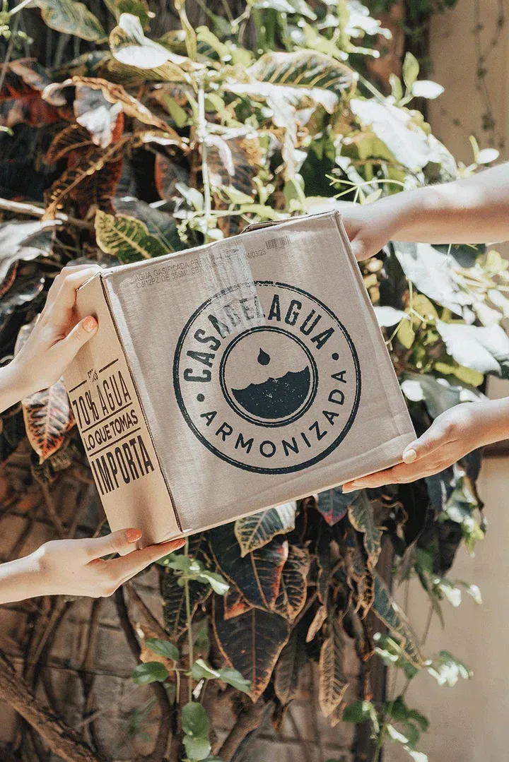 Hands holding a Casa del Agua Armonizada branded jute package surrounded by green plants