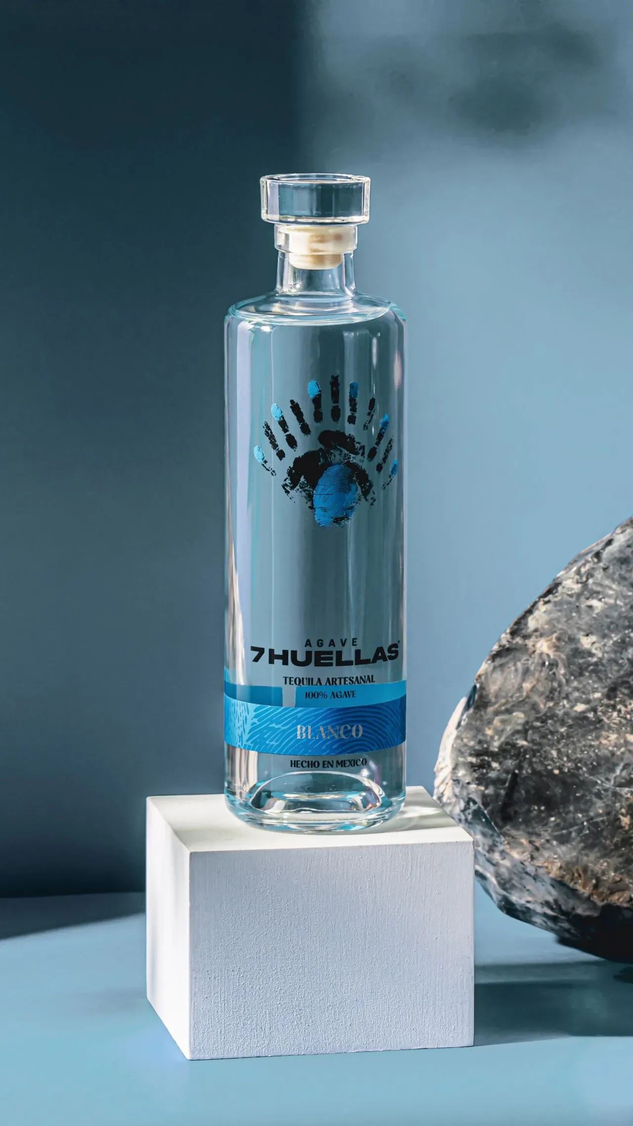 Blanco bottle on white pedestal with dark rock and blue background