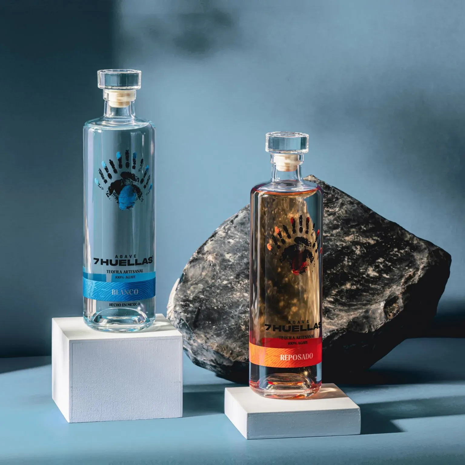 Blanco and Reposado bottles on white pedestals with dark rock and blue background