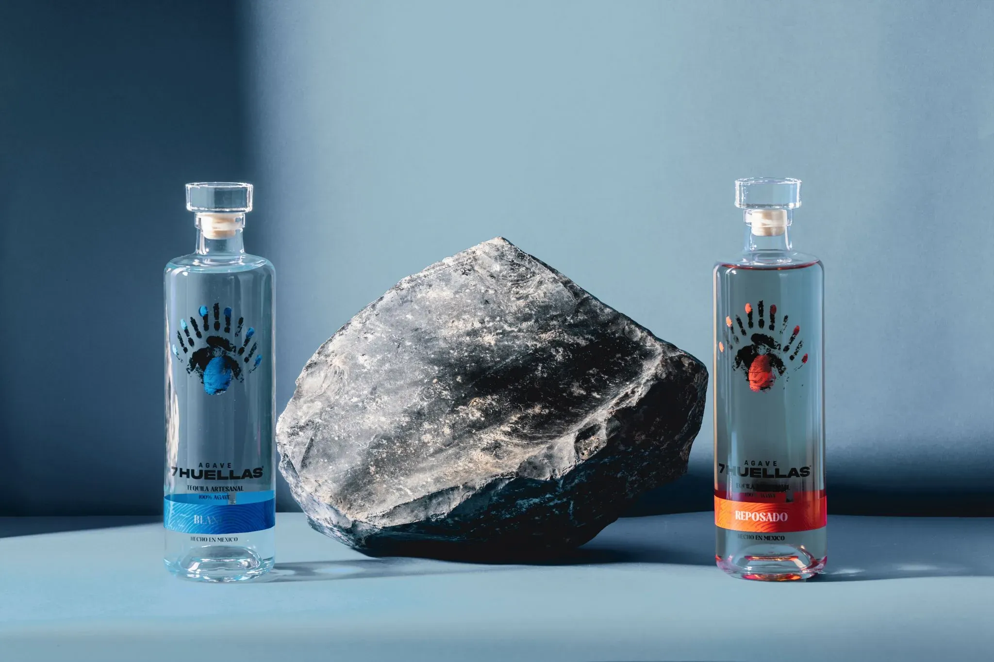 Blanco and Reposado bottles flanking dark rock on blue background