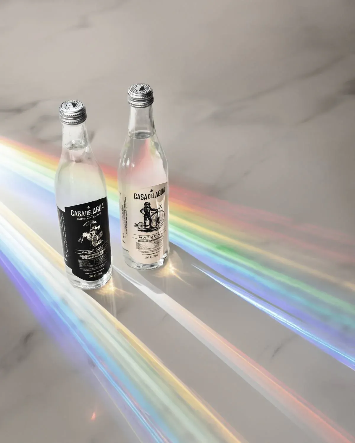 Natural and sparkling bottles on white marble surface with rainbow light prism reflections