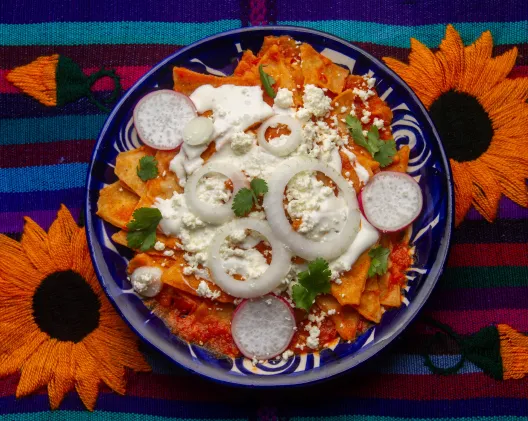 Chilaquiles rojos topped with crema, queso fresco, and radish slices on a blue Talavera plate
