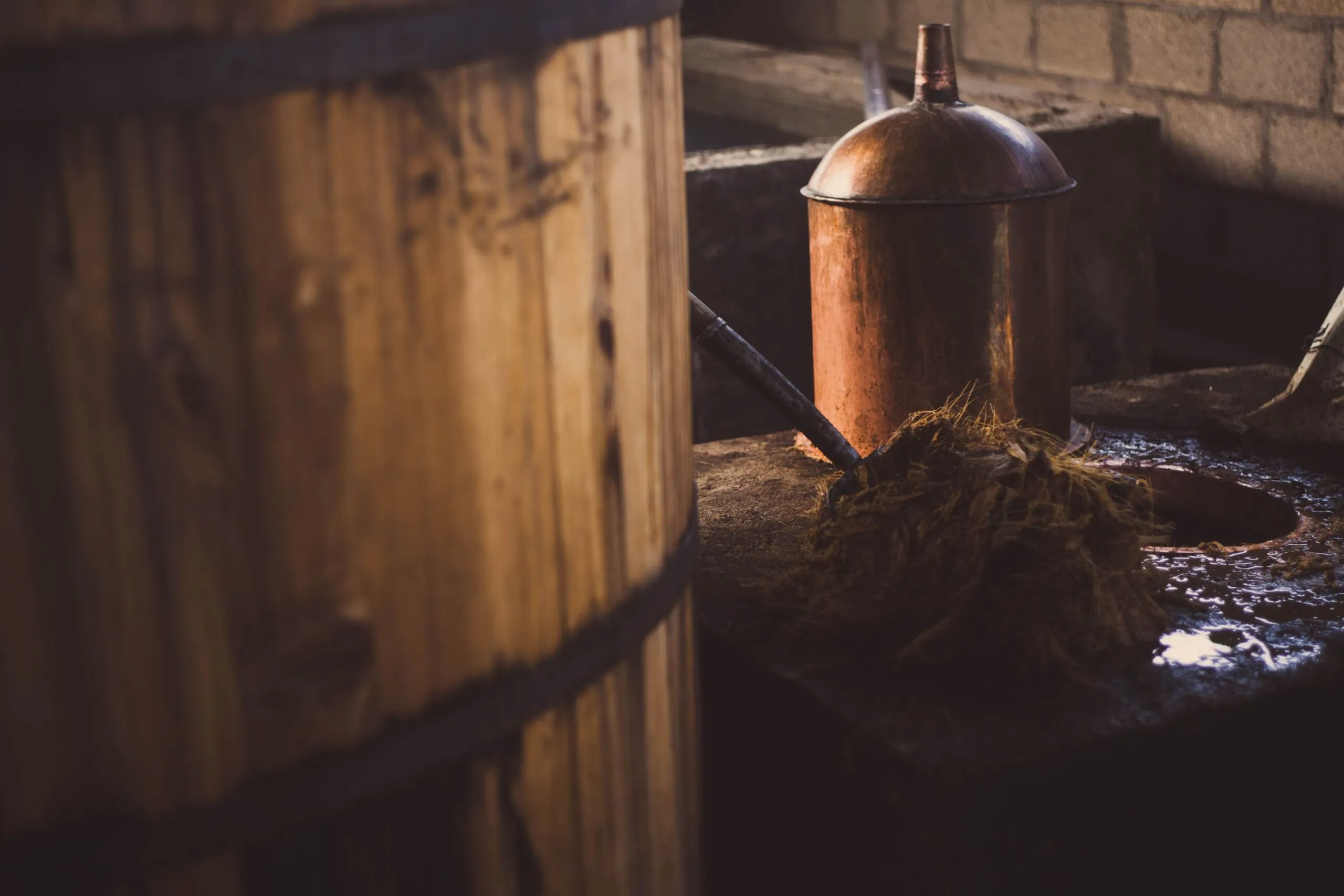 Copper still next to wooden fermentation vat inside palenque