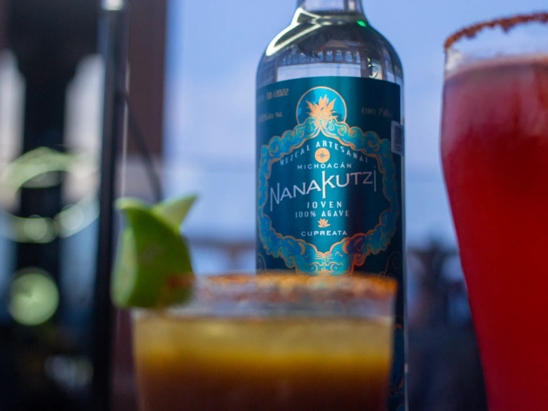 Close-up of Nanakutzi Cupreata label with cocktails at dusk