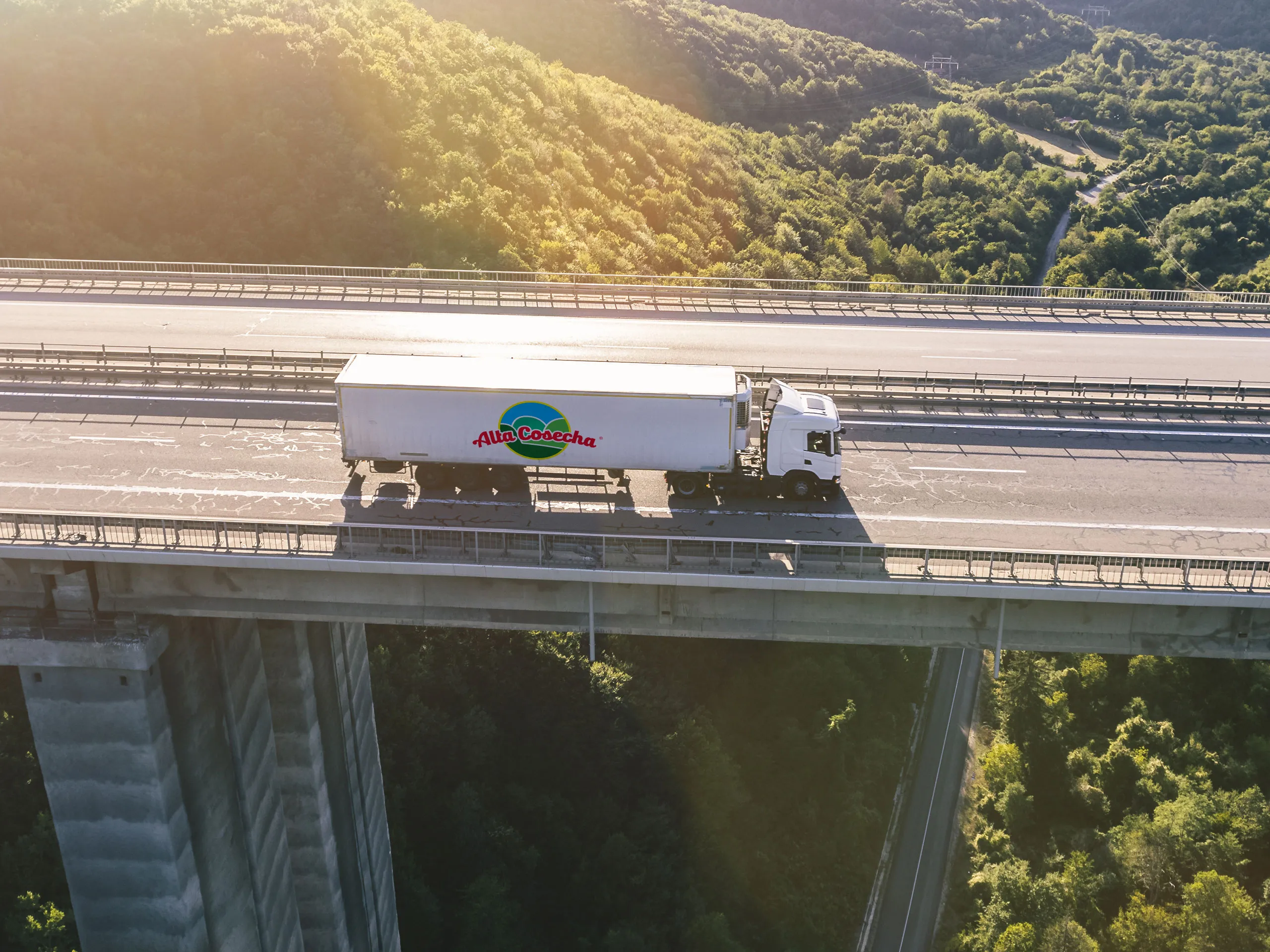 Aerial view of Alta Cosecha delivery truck crossing a bridge at sunset