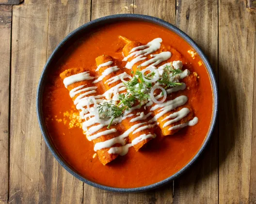 Enchiladas rojas drizzled with crema on a dark plate over wooden table