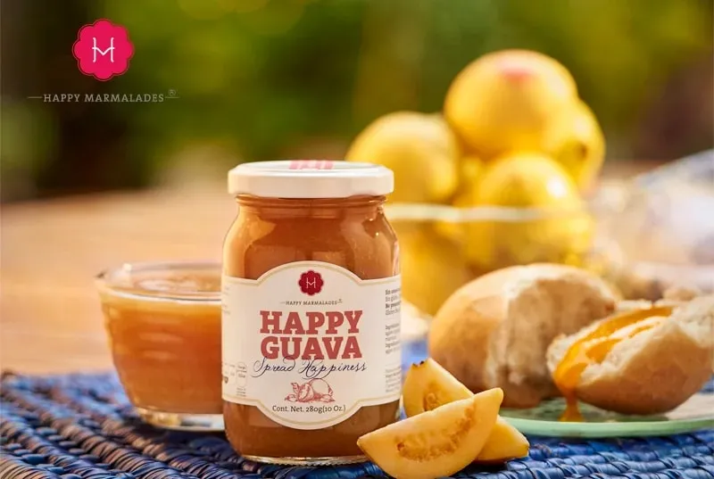 Happy Guava jar on blue woven mat with sliced guavas, bread, and garden backdrop