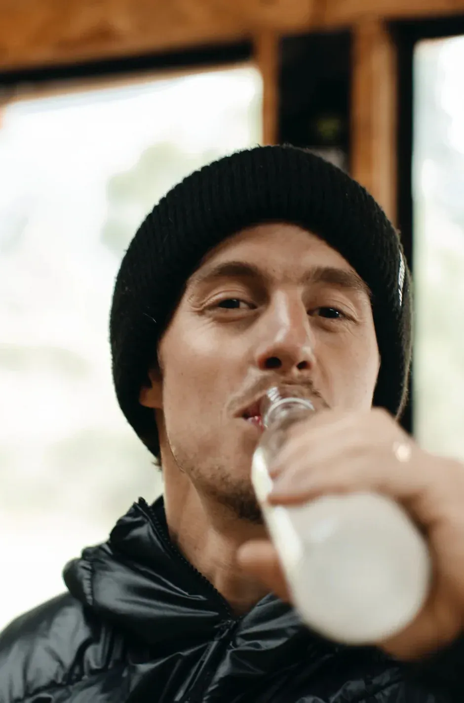 Man in black beanie and jacket drinking from a Casa del Agua bottle outdoors