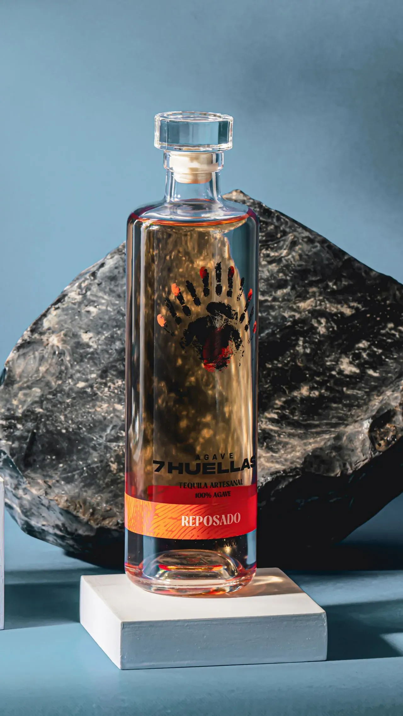 Reposado bottle on white pedestal with dark rock and blue background