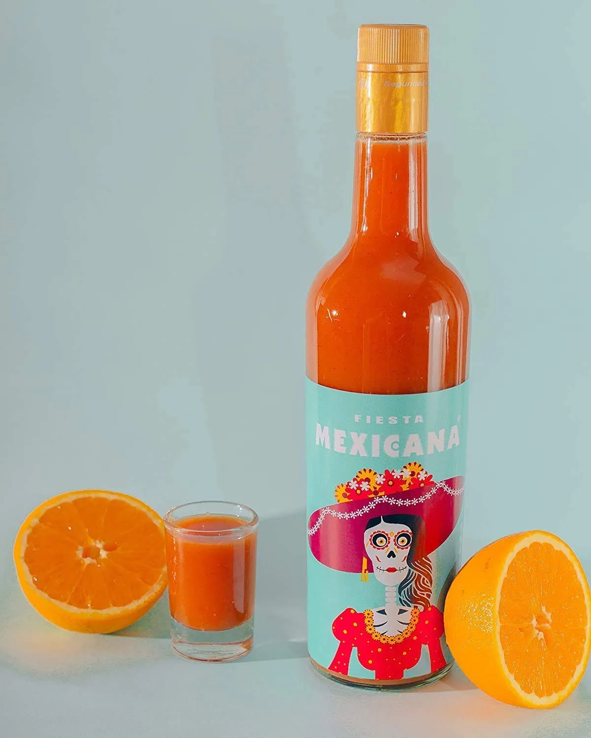 Sangrita 750ml bottle with fresh halved oranges and shot glass