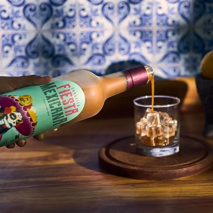 Sangrita being poured over ice on walnut counter with Talavera tiles