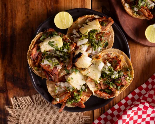 Tacos al pastor served on a dark plate with lime, top-down view