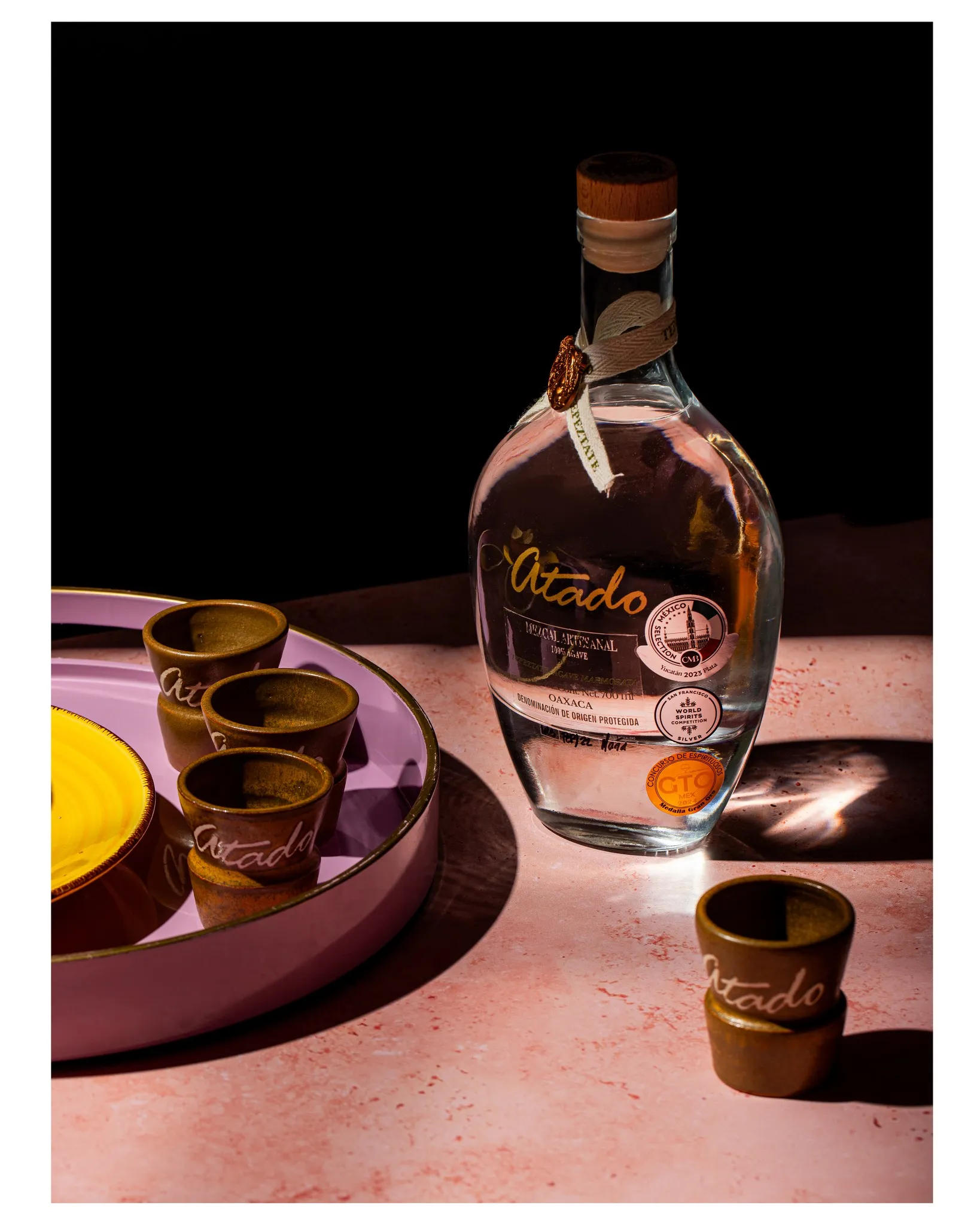 Tepeztate bottle with branded clay copitas on pink surface against black background