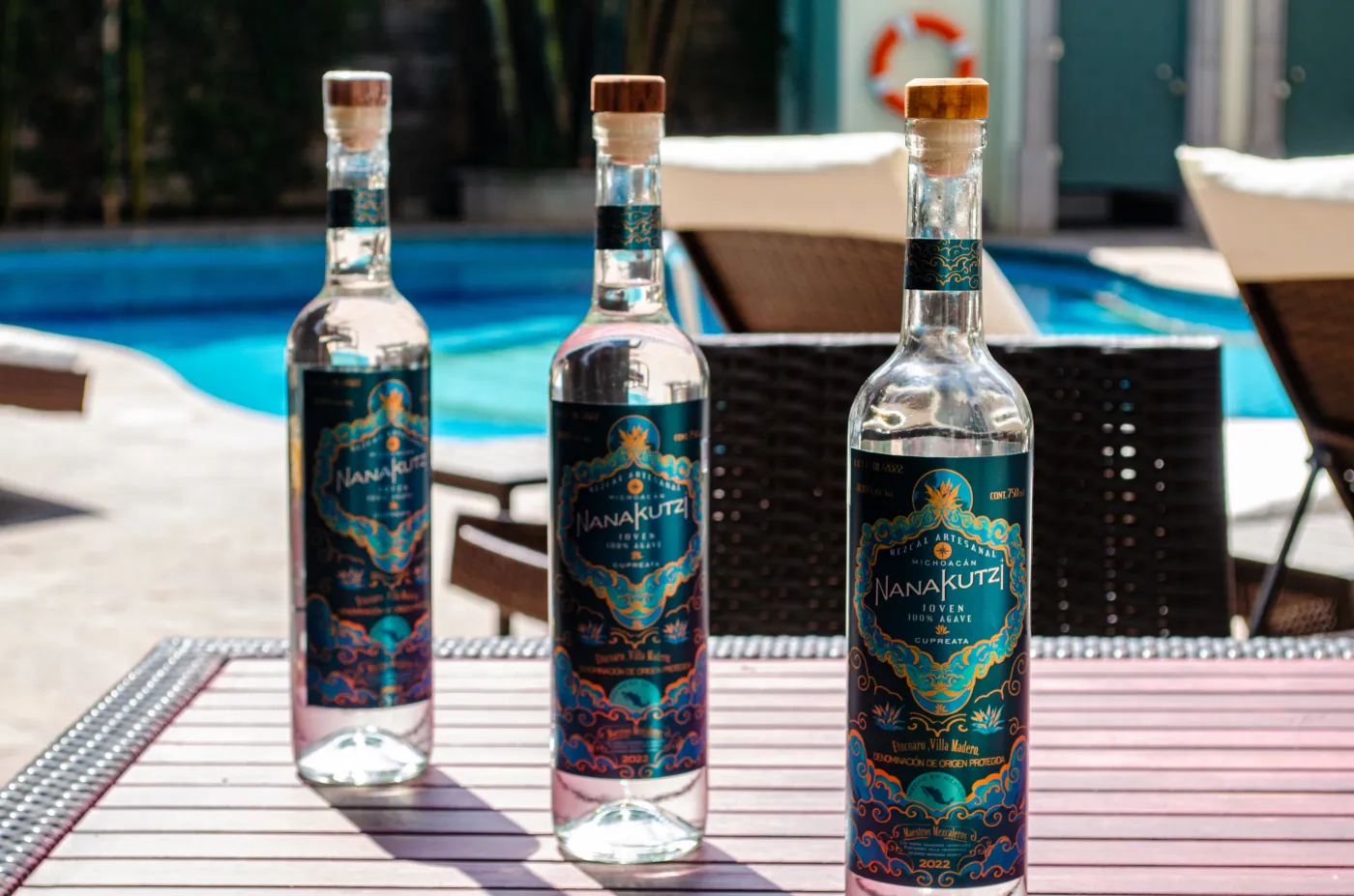 Three Nanakutzi mezcal bottles lined up on table by pool
