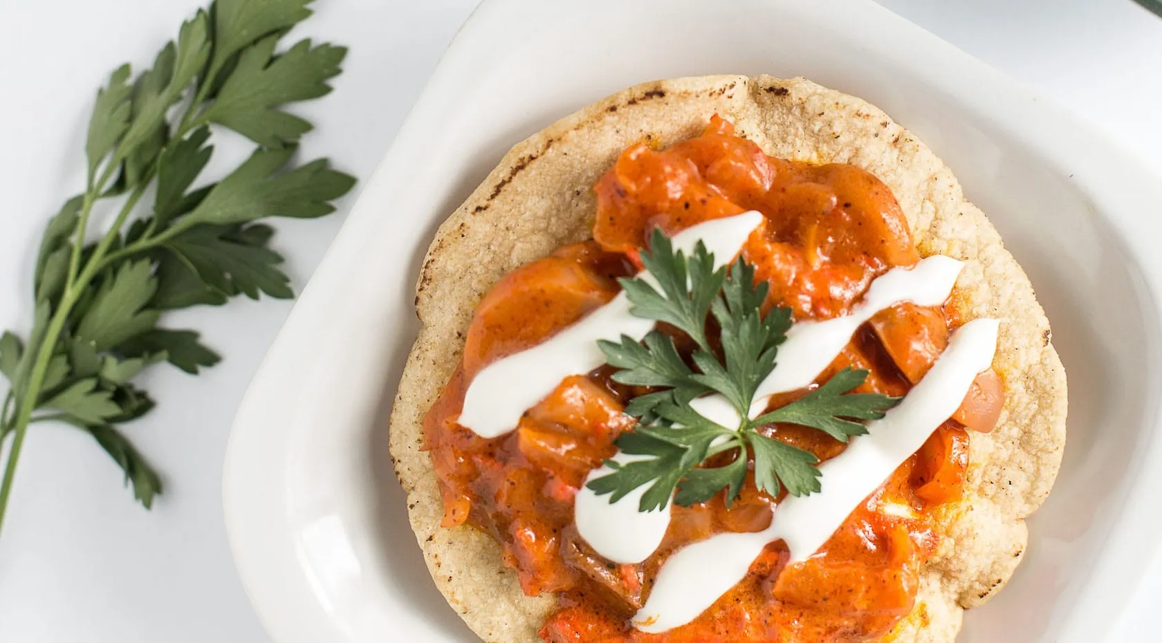 Crispy tostada topped with chicken tinga in chipotle sauce, drizzled with cream and garnished with fresh cilantro