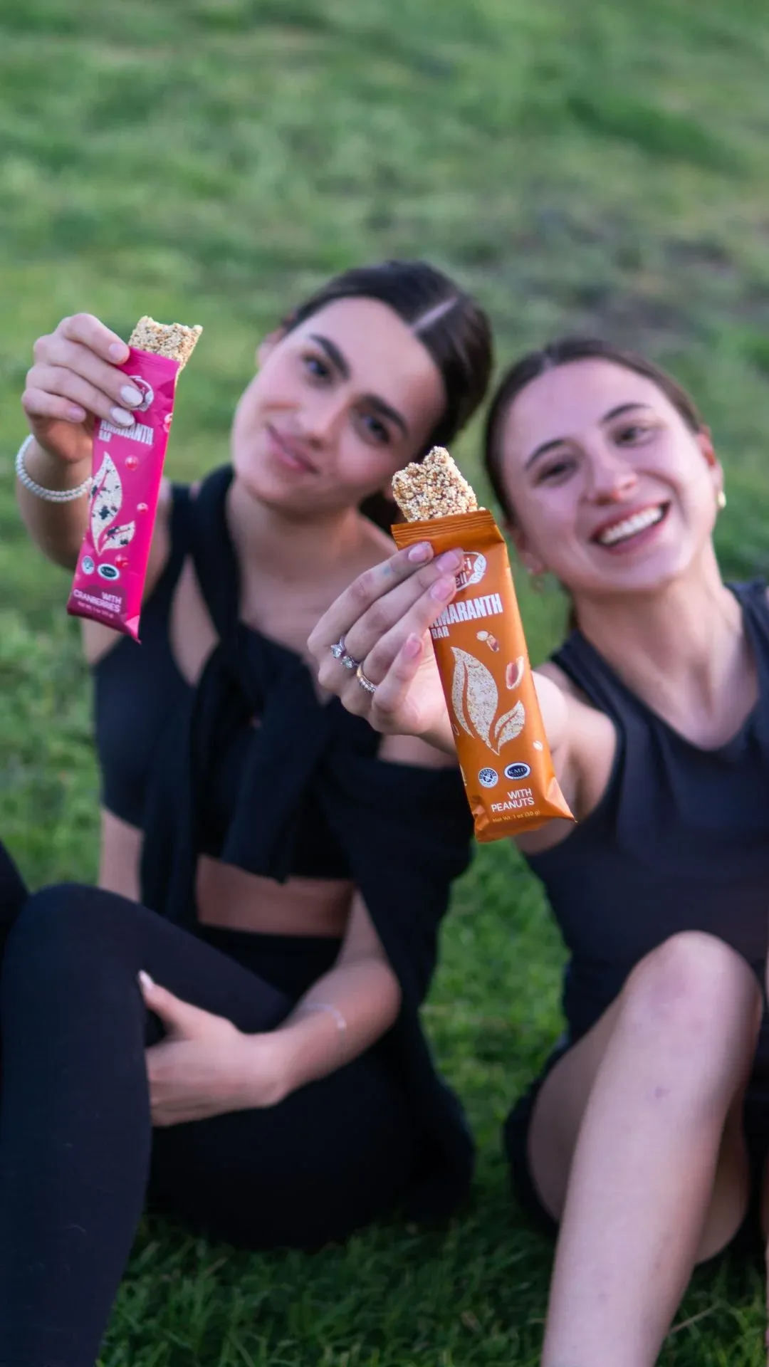 Two women on grass holding Nutri Well amaranth bars in portrait format